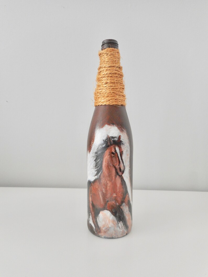 May include: A brown glass bottle with a brown horse painted on it. The bottle is wrapped with twine around the neck.