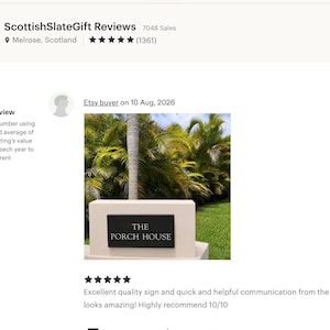 May include: A rectangular black slate sign with white engraved lettering that reads THE PORCH HOUSE. The sign is mounted horizontally on a light-colored, smooth, rectangular stone base positioned outdoors in front of green palm trees.
