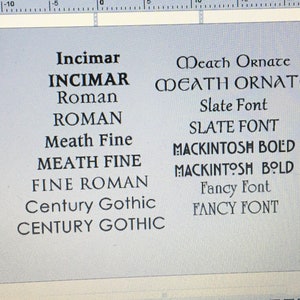 May include: A digital display showing a list of font names in black text on a light gray background. The list includes Incimar, Roman, Meath Fine, Fine Roman, Century Gothic, Meath Ornate, Slate Font, Mackintosh Bold, and Fancy Font in various styles.