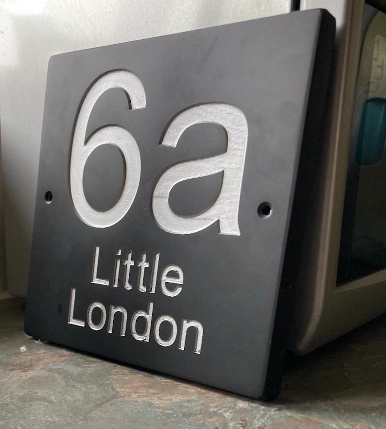 May include: A rectangular dark gray slate house sign featuring the engraved white text 6a and the words Little London below it. The sign has two circular mounting holes on the left and right sides, with a smooth, matte finish and clean edges.