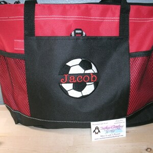 May include: Red and black tote bag with a soccer ball and the name "Jacob" embroidered on the front. The bag has a mesh pocket on the side.