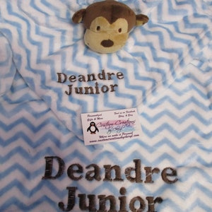 May include: A blue and white chevron baby blanket with a brown monkey plush toy. The blanket is personalized with the name "Deandre Junior".