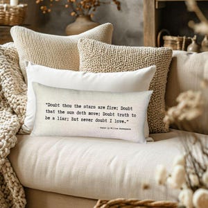 May include: A white pillow with a black and white quote from Shakespeare's Hamlet: "Doubt thou the stars are fire; Doubt that the sun doth move; Doubt truth to be a liar; But never doubt I love." The pillow is on a beige couch with other pillows.