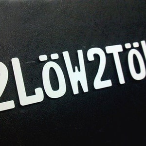 May include: White letters on a black background spell out "2LÖW2TÖW".