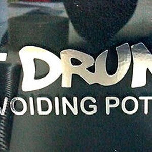 May include: A black and white sticker with the text "Not Drunk Just Avoiding Potholes" in a stylized font.