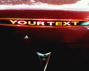 May include: A red car with a black trim piece on the back. The trim piece has the words "YOUR TEXT" in yellow letters.