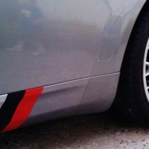 May include: Silver car with a black tire and a silver rim. The car's side panel features a decorative stripe design with gray, black, and red colors. The wheel is a multi-spoke design.