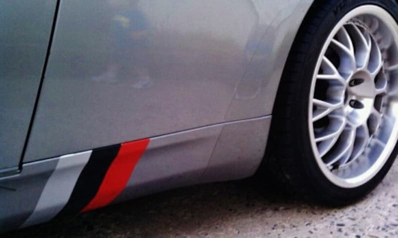 May include: Silver car with a black tire and a silver rim. The car's side panel features a decorative stripe design with gray, black, and red colors. The wheel is a multi-spoke design.