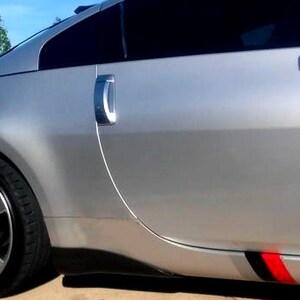 May include: Silver sports car with tinted windows, a rear spoiler, and a black and red accent stripe. The car has a shiny, metallic finish and a low profile. The alloy wheels have a multi-spoke design.