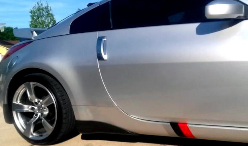 May include: Silver sports car with tinted windows, a rear spoiler, and a black and red accent stripe. The car has a shiny, metallic finish and a low profile. The alloy wheels have a multi-spoke design.