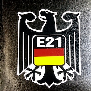 May include: Black and white sticker of a German eagle with a red, yellow, and black German flag and the text "E21" on a black background.