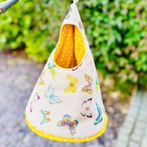 May include: A hanging fabric pouch with a yellow and white butterfly print. The pouch is lined with yellow fabric and has a yellow trim. It is hanging from a clothesline.