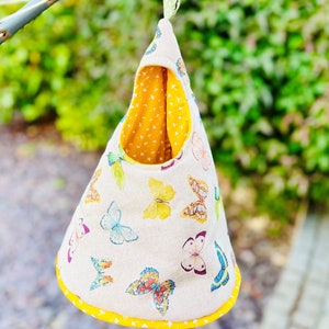 May include: A hanging fabric pouch with a yellow and white butterfly print. The pouch is lined with yellow fabric and has a yellow trim. It is hanging from a clothesline.