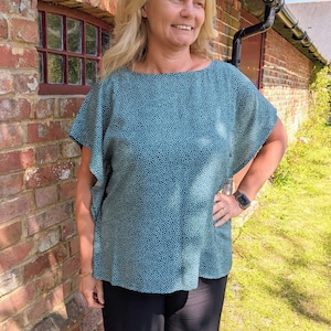 May include: A teal blue top with a white polka dot pattern. The top has a boat neck and short sleeves.