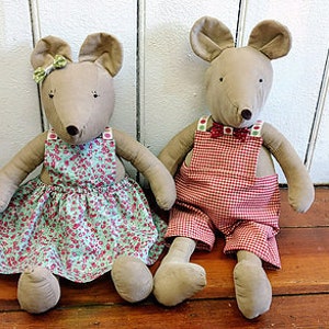 May include: Two plush mouse toys, one wearing a green floral dress and the other wearing red and white checkered overalls.