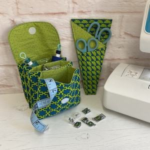 May include: A green and blue fabric sewing kit with multiple pockets and compartments. The kit includes a tape measure, scissors, and sewing machine feet.