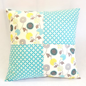 May include: A square cushion with a patchwork design. The cushion is made of four different fabrics, each with a different pattern. The fabrics are white with a floral pattern, turquoise with a geometric pattern, and white with a floral pattern. The cushion is perfect for adding a touch of colour and style to any room.