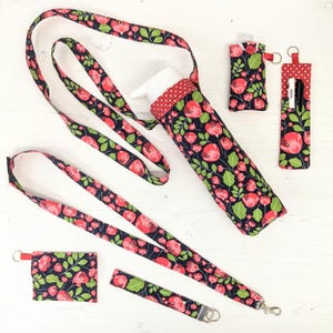 May include: A set of three fabric pouches with a floral print. The pouches are black with red flowers and green leaves. The pouches are attached to a black and red lanyard with a floral print. The pouches are perfect for carrying small items like keys, lip balm, or hand sanitizer.