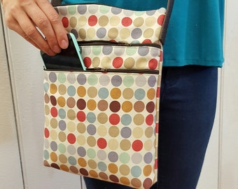 May include: A beige crossbody bag with a brown strap and a multi-colored polka dot pattern. The bag has two zippered compartments and a phone pocket.