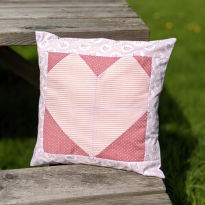 May include: A pink and red heart-shaped cushion with a floral pattern. The cushion is made of fabric and has a soft, quilted texture.