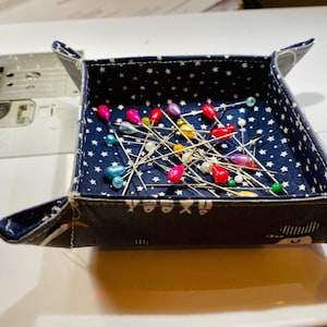 May include: A blue fabric pincushion with white stars and a fish pattern. The pincushion is filled with colorful sewing pins.