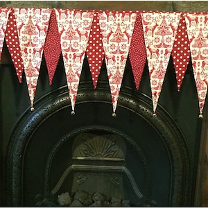 May include: A red and white Christmas banner with a Scandinavian pattern hangs above a black fireplace. The banner is made of fabric and has a scalloped edge. Each triangle has a bell at the bottom.