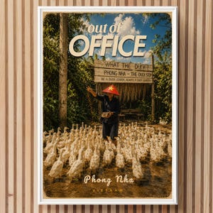 Può includere: Un poster incorniciato che mostra una persona con un cappello conico rosso che nutre un grande stormo di anatre bianche in un ambiente rurale. Il testo recita "out of OFFICE" in alto e "WHAT THE DUCK? PHONG NHA - THE DUCK STOP" e "Phong Nha VIETNAM" in basso.