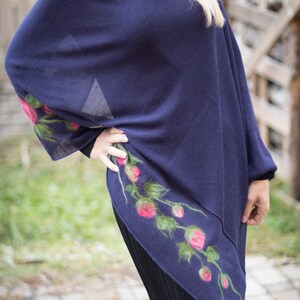 May include: A navy blue poncho with a floral design featuring pink roses and green leaves. The poncho is made of a soft, lightweight fabric and has a relaxed fit.