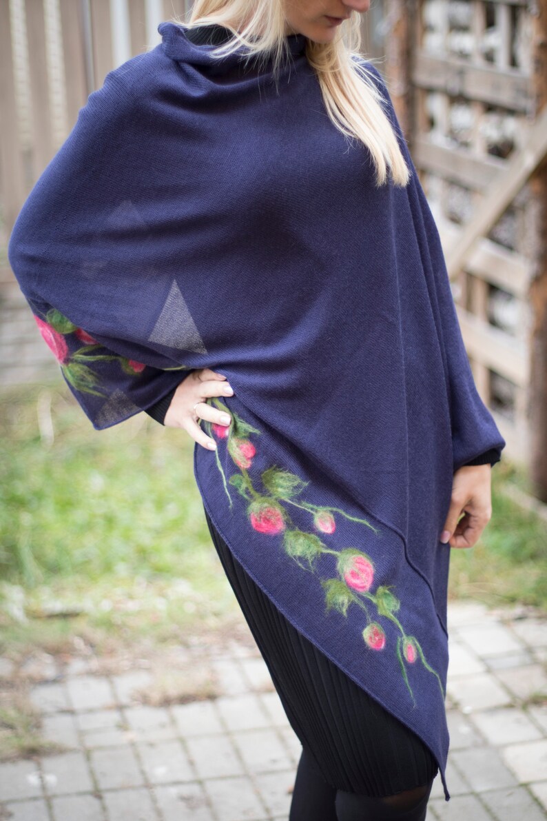 May include: A navy blue poncho with a floral design featuring pink roses and green leaves. The poncho is made of a soft, lightweight fabric and has a relaxed fit.