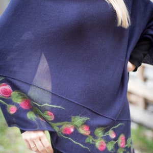 May include: A navy blue knitted poncho with a floral design featuring pink and green felt flowers.