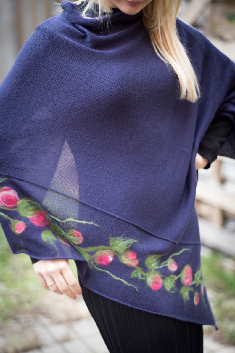 May include: A navy blue knitted poncho with a floral design featuring pink and green felt flowers.