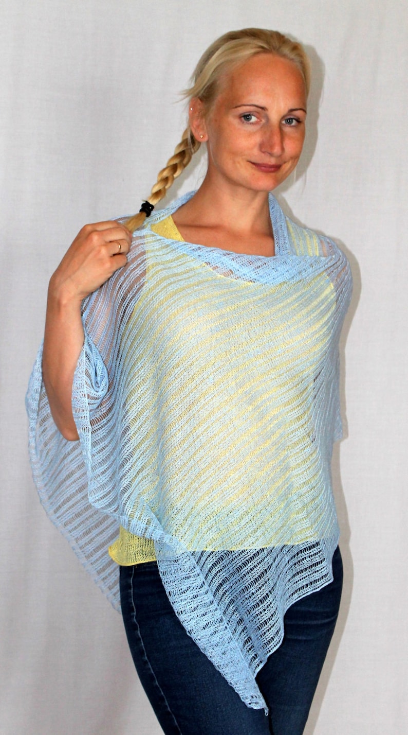 May include: A light blue knitted poncho with a yellow under layer. The poncho has a loose fit and a diagonal striped pattern.