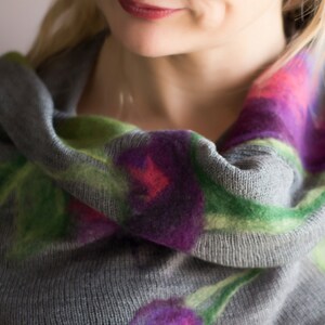 May include: A gray cowl neck sweater with a floral pattern in shades of green, purple, and pink.