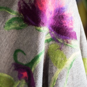 May include: A gray knitted fabric with a floral design. The flowers are made of felt and are in shades of pink, purple, and green.