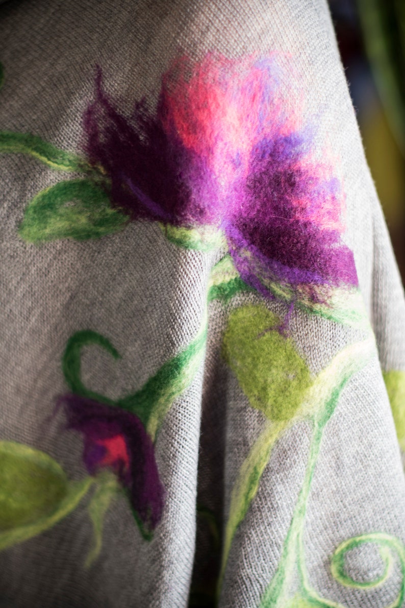 May include: A gray knitted fabric with a floral design. The flowers are made of felt and are in shades of pink, purple, and green.