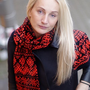 以下が含まれることがあります： 黒のジャケットに赤と黒の模様の入ったスカーフを巻いた、長い金髪の女性