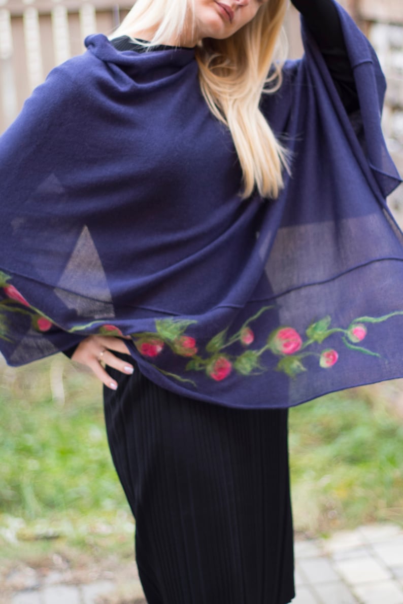 May include: A navy blue shawl with a floral design featuring pink flowers and green leaves. The shawl is made of a soft, lightweight fabric and is perfect for layering.