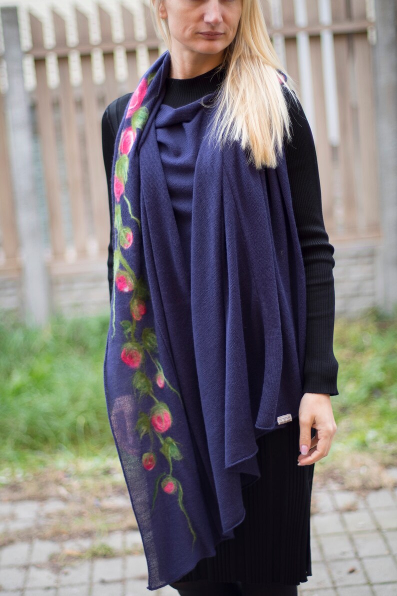 May include: A navy blue scarf with a floral design featuring pink flowers and green leaves. The scarf is made of a soft, lightweight material and is perfect for adding a touch of elegance to any outfit.