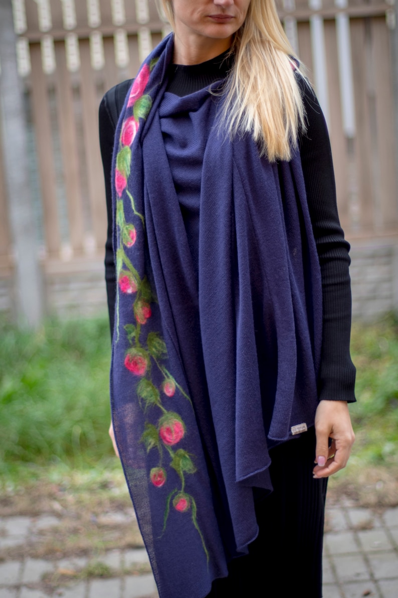 May include: A navy blue scarf with a floral design featuring pink roses and green leaves. The scarf is made of a soft, lightweight material and is perfect for adding a touch of elegance to any outfit.