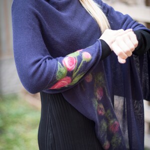 May include: A navy blue knitted poncho with a floral design on the sleeve. The flowers are pink, green, and white.