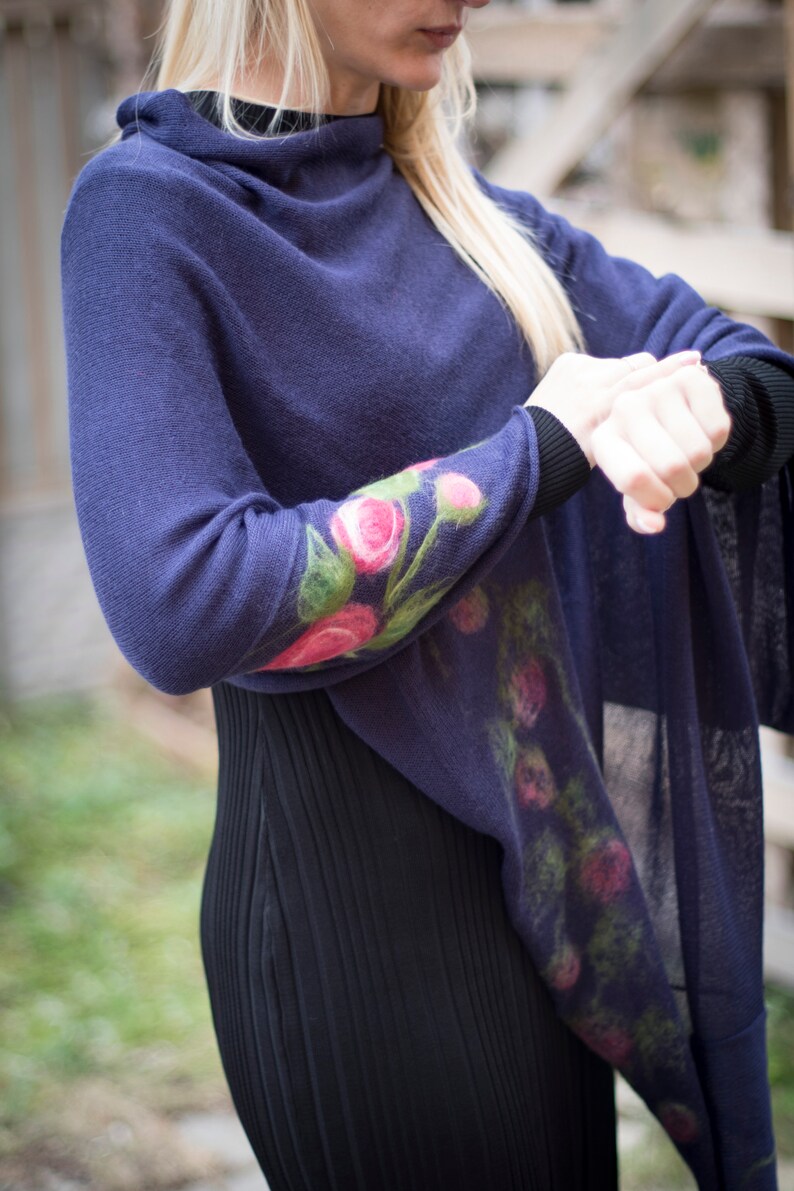 May include: A navy blue knitted poncho with a floral design on the sleeve. The flowers are pink, green, and white.