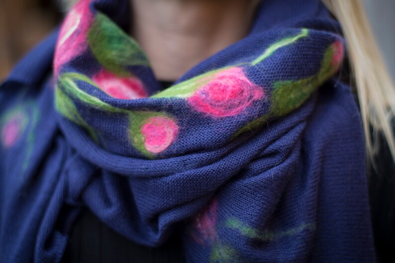 May include: A blue knitted scarf with pink and green floral embroidery.