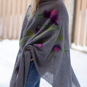 May include: A gray poncho with a floral design featuring purple, pink, and green flowers. The poncho is made of a soft, lightweight fabric and has a flowing, asymmetrical hemline.