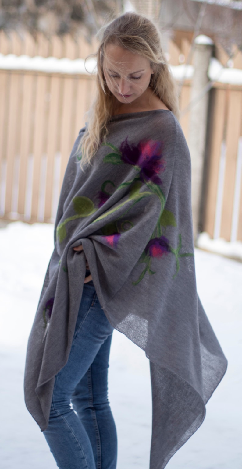 May include: A gray poncho with a floral design featuring purple, pink, and green flowers. The poncho is made of a soft, lightweight fabric and has a flowing, asymmetrical hemline.