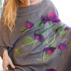 May include: A gray knitted poncho with a floral design featuring purple, pink, and green flowers. The poncho is made of a soft, lightweight fabric and has a relaxed fit.