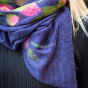 May include: A purple knitted scarf with a floral design. The flowers are pink, green, and white.