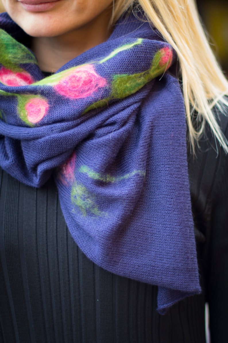 May include: A purple knitted scarf with a floral design. The flowers are pink, green, and white.