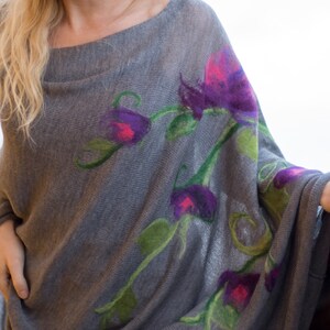 May include: A gray knitted poncho with a floral design featuring purple, pink, and green flowers.