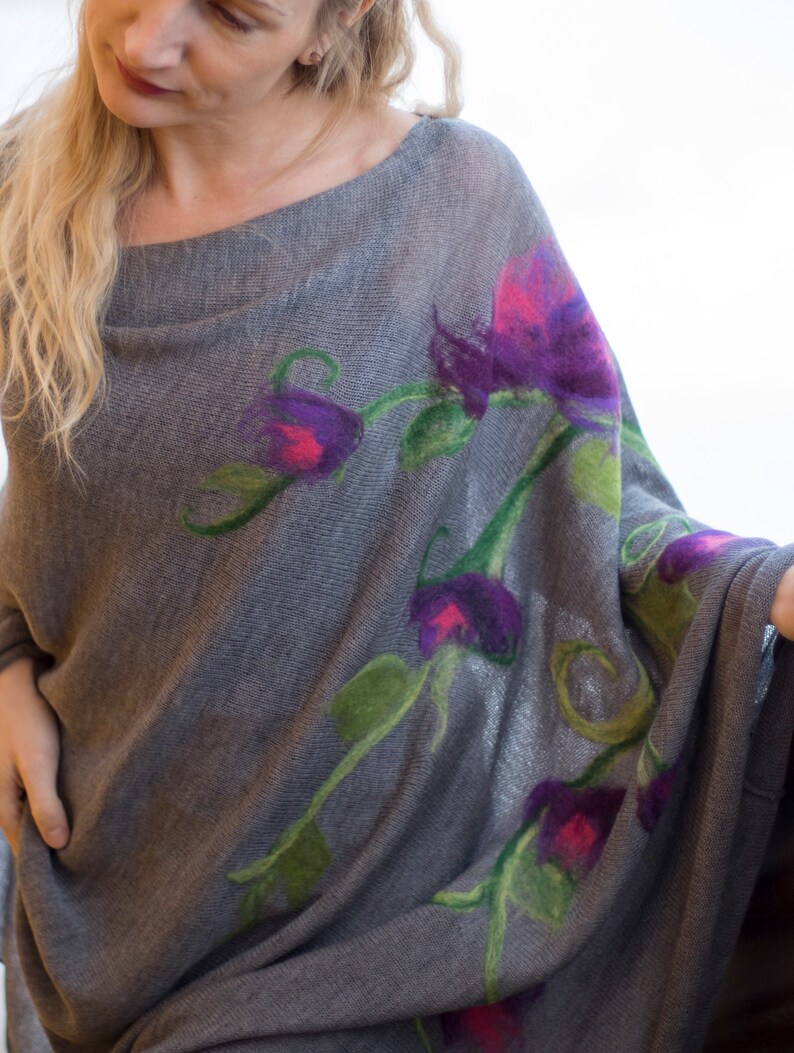 May include: A gray knitted poncho with a floral design featuring purple, pink, and green flowers.