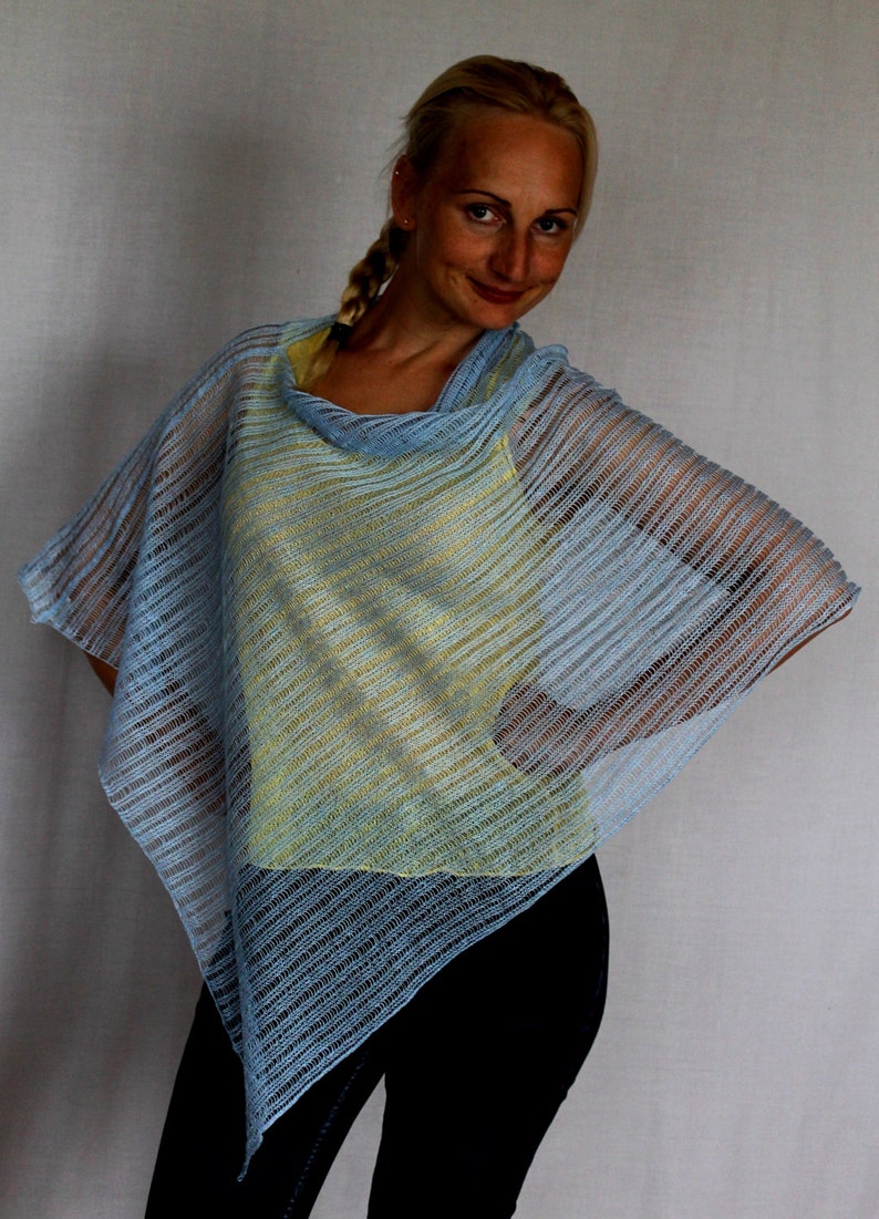 May include: A light blue knitted poncho with a yellow and blue striped pattern. The poncho is worn over a yellow tank top and black pants.